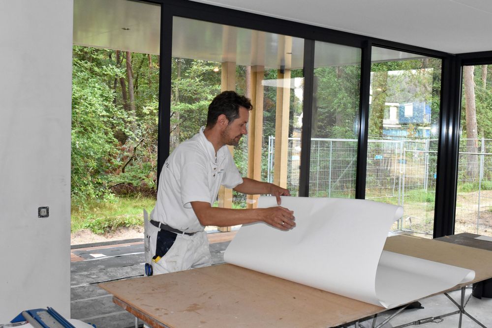 Roland Visser rolt een baan renovlies uit op de werktafel in een nieuwbouwwoning